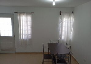 A room with a dining table, chairs, a window with curtains, a door, and a ceiling light. - Casa 2 recámaras zona aeropuerto clima total (Pesquería)