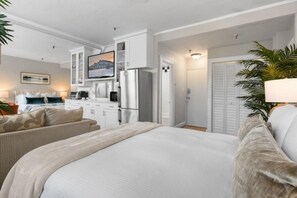 Quarto de hotel com cama, escrivaninha, geladeira, televisão e porta que dá para outro cômodo.