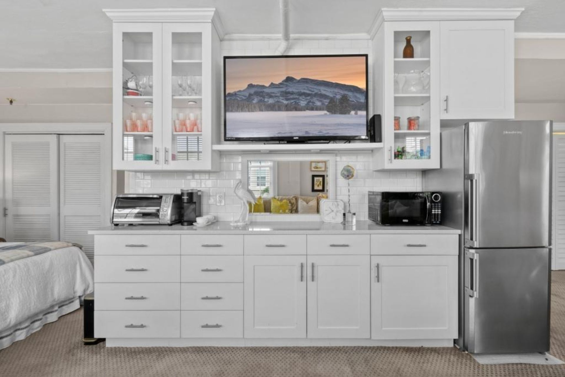 A modern kitchen with a built-in TV, stainless steel appliances, and white cabinetry.