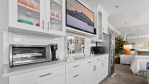 Una cocina moderna con horno empotrado, microondas y refrigerador, televisor de pantalla plana y armarios blancos.