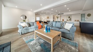 A modern living room with a sofa set, a coffee table, and a kitchen area in the background. - Level Up Henley - Modern Comfort near Beach & Dining (Henley Beach)