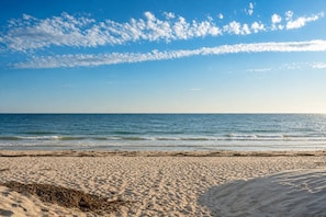 A beach with sand and sea under a partly cloudy sky.