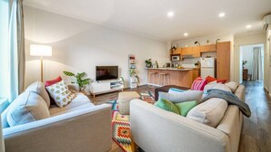 Una sala de estar moderna con un juego de sofá, televisión y una cocina al fondo.