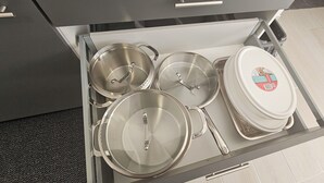 Un cajón de cocina con utensilios de acero inoxidable, incluyendo ollas, sartenes y una olla grande con tapa.