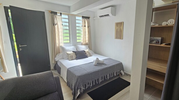 Un dormitorio con cama, mesita de noche, silla, armario y ventana con cortinas.