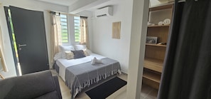 A bedroom with a bed, a bedside table, a chair, a wardrobe, and a window with curtains.