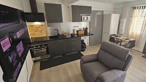 Una cocina compacta con electrodomésticos modernos, un comedor con una mesa pequeña y sillas, y un sofá gris.