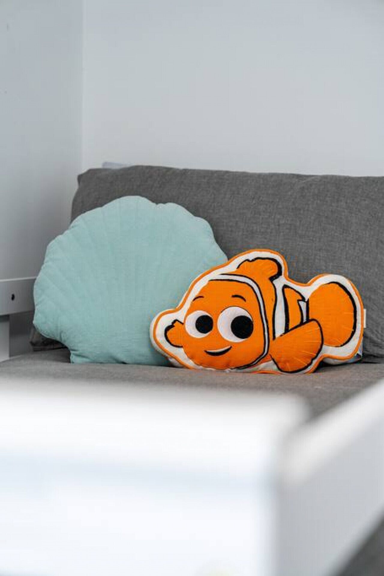 A grey sofa with a teal pillow and an orange plush toy.