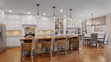 Une cuisine avec des meubles blancs, un îlot central doté de tabourets et des luminaires suspendus.