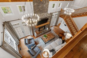 A spacious living room with a stone fireplace, wooden staircase, and a chandelier. - Peaceful Lake House, Hot Tub & Private Dock! (wedowee)
