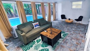 A living room with a sofa, a coffee table, and a pool view. - Private Oasis w/ Pool, 7 min to Beach, Pool Table (Hollywood)