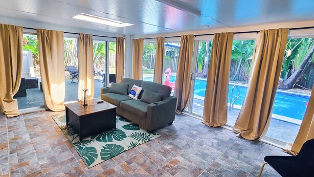 A spacious living area with a sofa, coffee table, and a view of a swimming pool. - Private Oasis w/ Pool, 7 min to Beach, Pool Table (Hollywood)