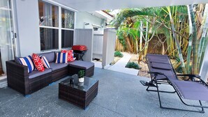 A covered patio with a dark wicker sofa, a glass coffee table, and a lounge chair. - Private Oasis w/ Pool, 7 min to Beach, Pool Table (Hollywood)
