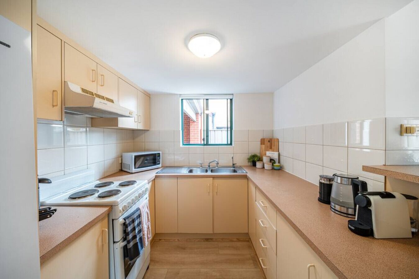 Uma cozinha compacta com fogão, micro-ondas, pia e uma janela.