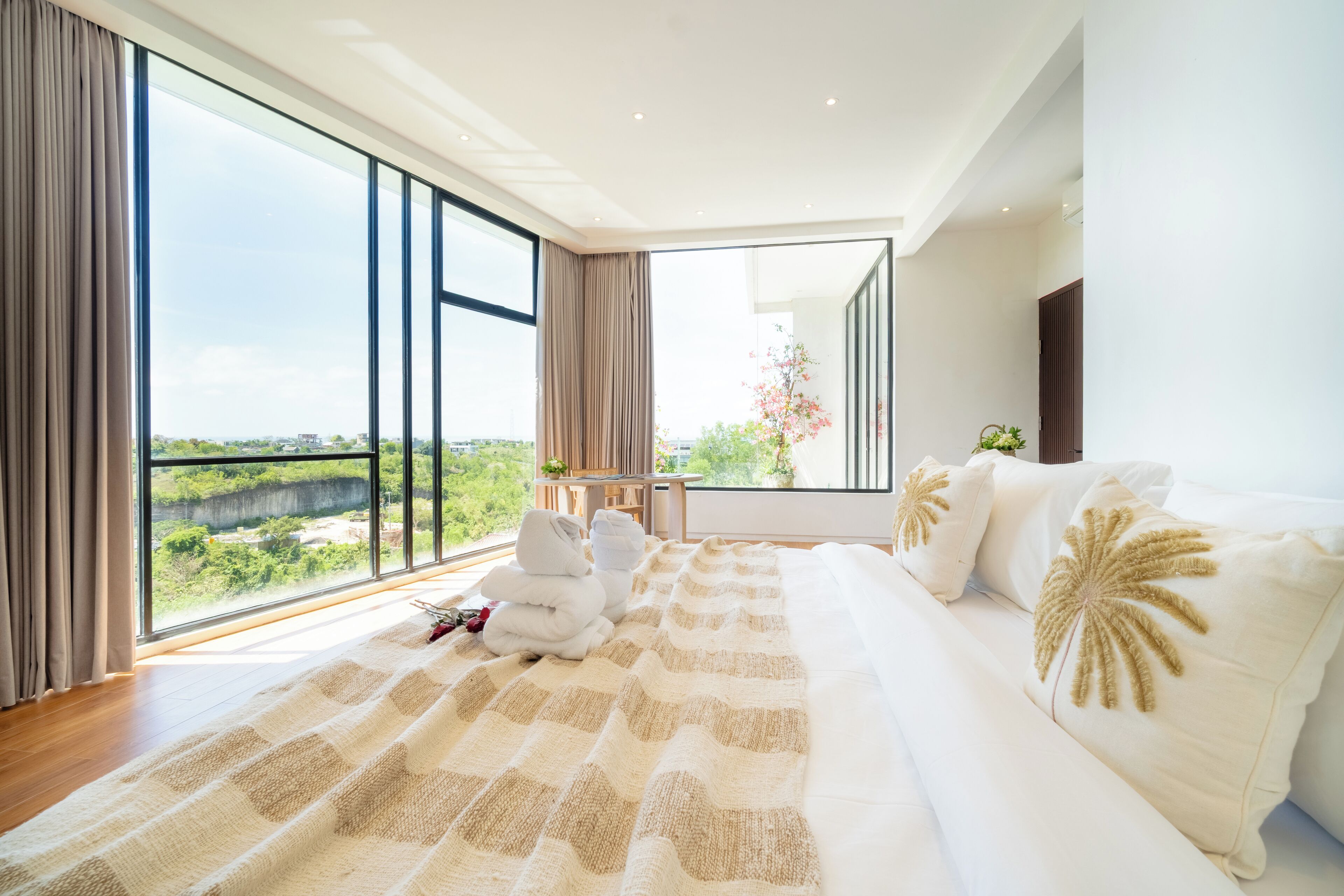 A modern bedroom with a large window, a bed with white bedding, and a view of greenery outside.