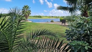 A view of a golf course with a water body, surrounded by lush greenery and palm trees. - Upscale Blue Bay Golf & Beach Suite – Gated Resort – 5 Min Walk to Beach (Sint Michiel)