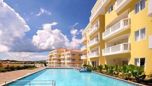 A hotel with a swimming pool, multiple balconies, and a clear sky. - Upscale Blue Bay Golf & Beach Suite – Gated Resort – 5 Min Walk to Beach (Sint Michiel)