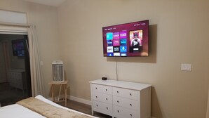 Ein Schlafzimmer mit einem Bett, einem an der Wand montierten Fernseher, der verschiedene Streaming-Dienste anzeigt, einem Heizgerät und einer weißen Kommode.