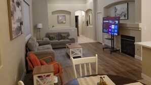 Ein Wohnzimmer mit einer Couch, Sesseln, einem Fernseher und einem Kamin.