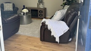 Un salon avec un canapé en cuir, un fauteuil à motifs, une petite table d’appoint, un téléviseur à écran plat et une plante décorative.