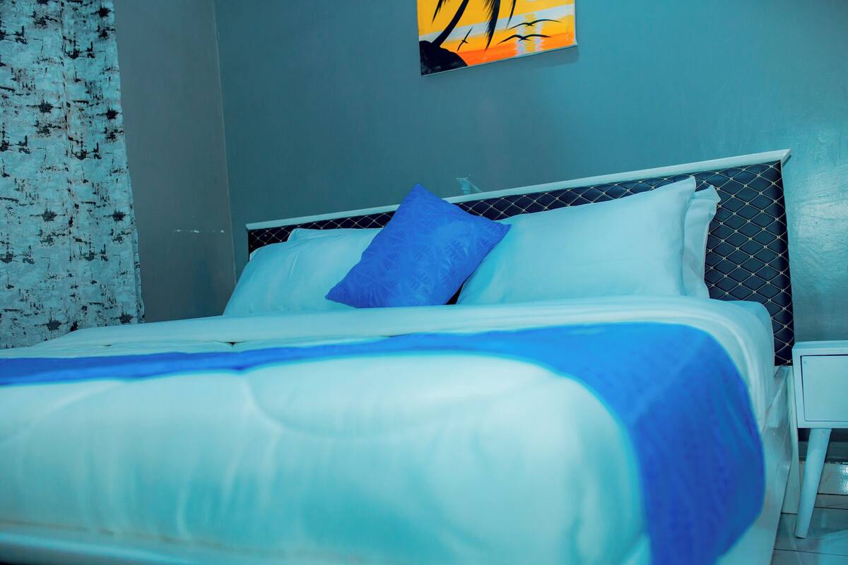 A bed with white and blue bedding, a blue pillow, and a white nightstand with a lamp.