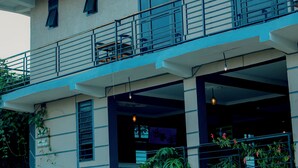 Un edificio de varios pisos con un balcón en el nivel superior, un área de entrada cubierta y un letrero que indica un restaurante.