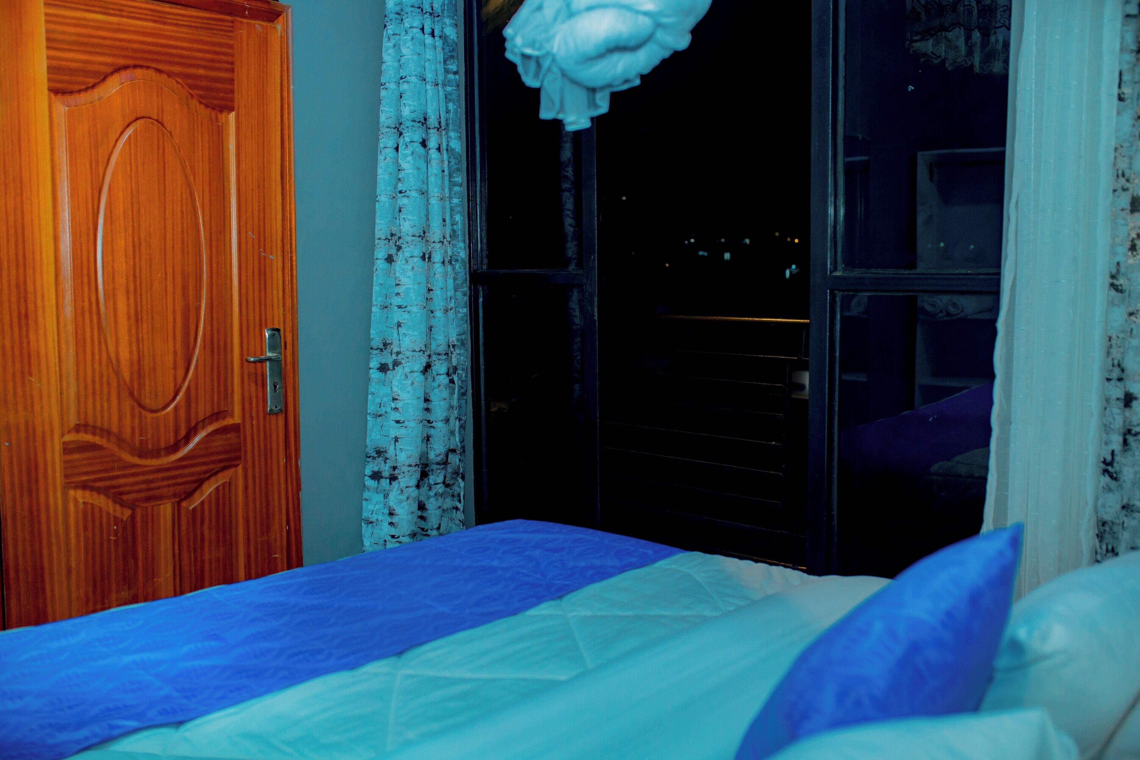 A bedroom with a wooden door, a window with a view of the outside, and a bed with a blue and white bedspread.