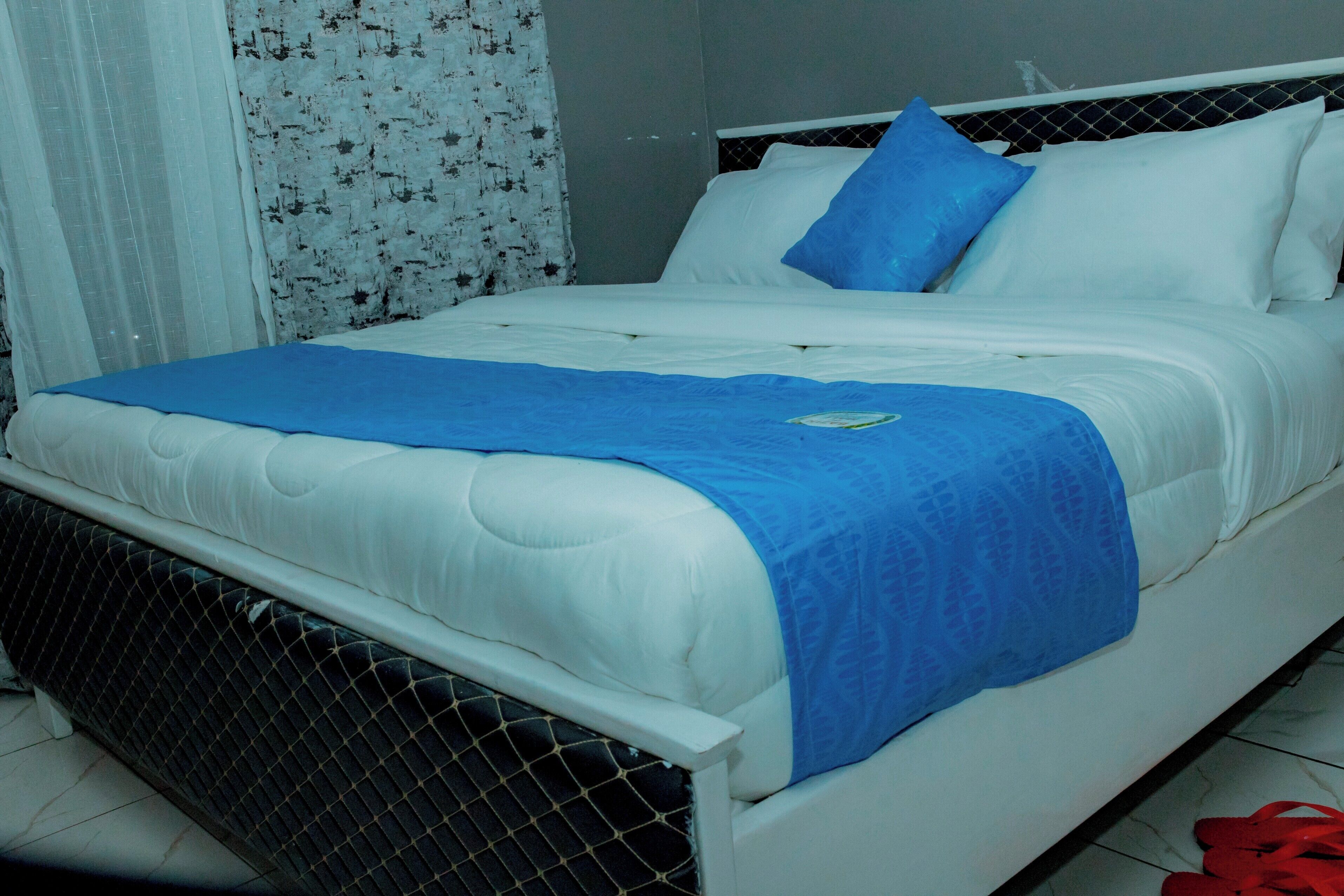 Una cama con ropa de cama blanca, una manta azul y una almohada.