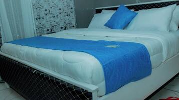 Una cama con ropa de cama blanca, una manta azul y una almohada.