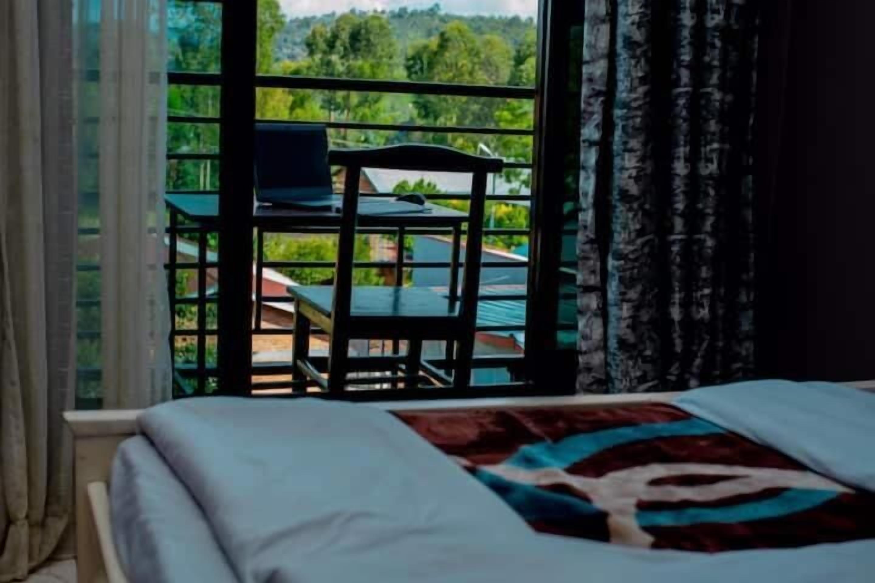 A bedroom with a bed, a window with a view of greenery and a table outside.