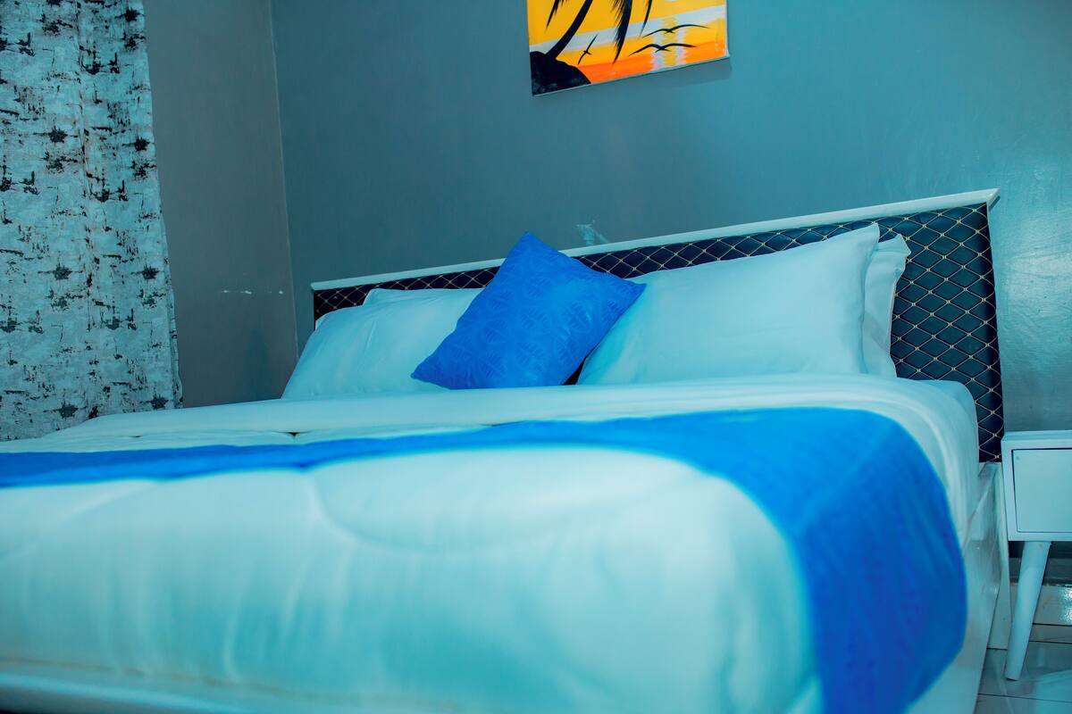 A neatly made bed with white and blue bedding, a small bedside table, and a wall with a geometric pattern.
