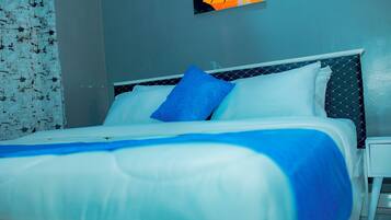 Una cama bien hecha con ropa de cama blanca y azul, una mesita de noche pequeña y una pared con un diseño geométrico.