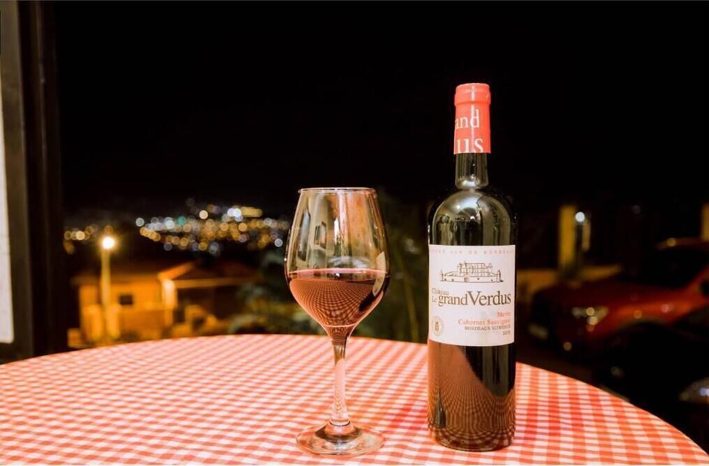 A bottle of Chateau Grand Verdus wine and a glass of wine on a table with a red and white checkered tablecloth.