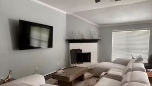 Un salon doté d’une cheminée, d’un téléviseur fixé au mur et d’un grand canapé d’angle.