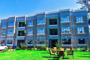 A multi-story residential building with a brick facade, large windows, and a well-maintained lawn with outdoor furniture.