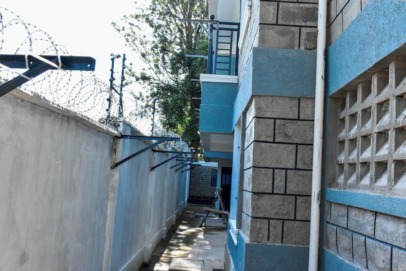 Un estrecho callejón con un muro de hormigón a un lado y un edificio azul al otro.