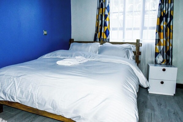 A neatly made bed with white linens, a wooden headboard, and a nightstand with drawers.