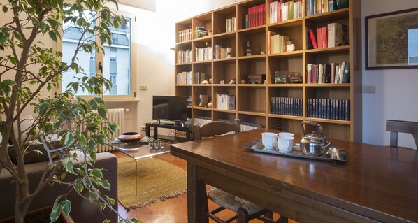 Una sala de estar acogedora con una estantería de madera, un televisor y un comedor con una mesa dispuesta para el té.