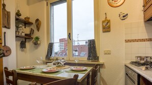 Eine Küche mit Esstisch für zwei Personen, einem fenster mit Vorhängen sowie verschiedenen Küchenutensilien und Dekoration an den Wänden.