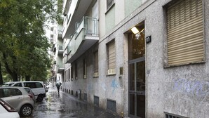 Eine schmale Stadtstraße mit parkenden Autos und einem Fußgänger. Die Gebäude haben Balkone und Fensterläden.