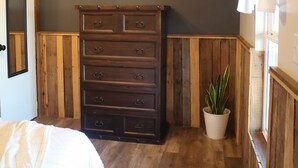 A bedroom with a wooden dresser, a ceiling fan, a potted plant, and a mirror on the wall.