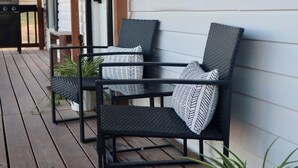 A wooden deck with two black wicker chairs and a potted plant.