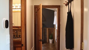 A hallway with wooden flooring, a door leading to a bathroom, a coat rack, and a potted plant.