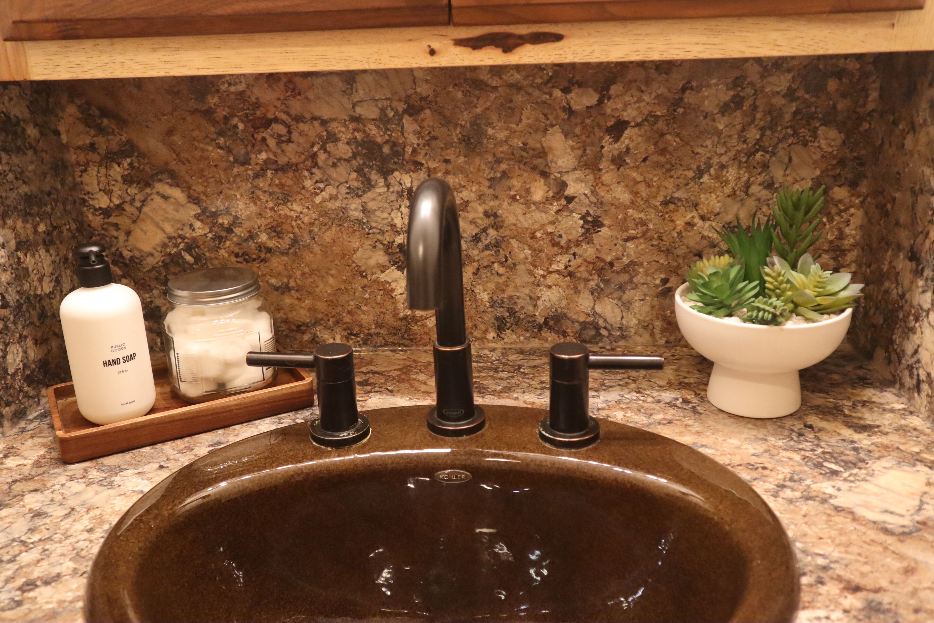 A kitchen sink with a granite countertop, a faucet, a soap dispenser, and a small potted plant.