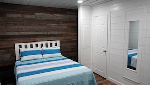 Ein Schlafzimmer mit Holzwand, einem Bett mit gestreifter Bettdecke, weißen Türen und einem Fenster mit Blick.