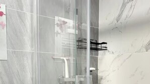 Een moderne badkamer met een douchecabine van glas, marmeren tegels en een witte wastafel.
