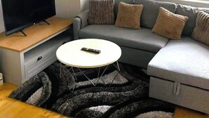 A modern living room with a grey sofa, a white coffee table, a TV on a wooden stand, and a black and grey rug. - Modern Flat/Central Croydon/Sleeps 4/Free Parking (Croydon)