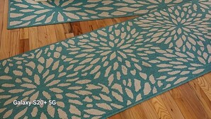 Un comedor con mesa de madera, sillas, una araña y un tapete estampado.