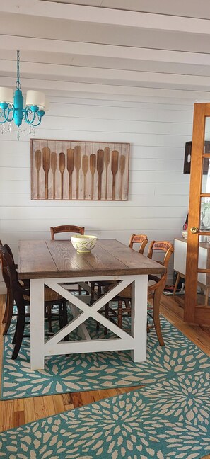 A dining area with a wooden table, chairs, a decorative wall piece, and a patterned rug.