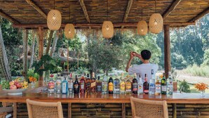 Un espace bar avec une table en bois, des chaises en osier et une variété de bouteilles d’alcool.